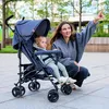 A woman and a baby are sitting on the ground next to a stroller. Produktbild-Vorschau