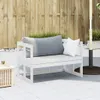 A white wooden garden bench with cushions on a tiled patio, with a wooden fence and greenery in the background. Náhled obrázku produktu