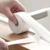 A hand is unrolling a roll of white sealing tape onto a wooden surface. Anteprima dell’immagine prodotto