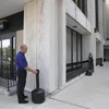 Two people are standing next to a building, one of them is interacting with a black stand-up ashtray. Voir les images du produit