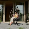 A woman sits in a hanging chair on a deck, reading a book. Produktbild-Vorschau