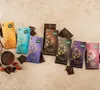 A collection of Naturata chocolate bars arranged on a textured surface, with some broken pieces of chocolate and strawberries scattered around. Náhled obrázku produktu