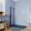 A modern bathroom with blue tiled walls, featuring a black framed glass shower enclosure with a dark gray shower tray. A wooden shelf unit with items on it is to the left, and a gold towel rack with a white towel is to the right. Produktbild-Vorschau