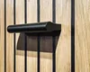 A close-up shot of a black door handle mounted on a wooden surface with black vertical accents. Produktbild-Vorschau