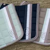 Three equestrian saddle pads are laid out on a sandy surface. Produktbild-Vorschau
