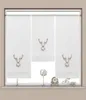 Three white roller blinds with embroidered deer heads are displayed in a window. Decorative items are on the windowsill below. Produktbild-Vorschau