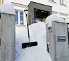 A snow shovel is leaning against a large pile of snow in front of a building entrance. Náhled obrázku produktu