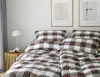 A neatly made bed with plaid bedding and two framed pictures on the wall above. Produktbild-Vorschau