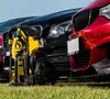 A yellow pressure washer and two cars (one red, one black) are parked on a grassy area. Produktbild-Vorschau
