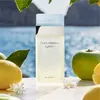 A bottle of Dolce & Gabbana Light Blue Eau de Toilette is displayed on a surface with lemons, apples, and small white flowers, with a blurred ocean and foliage in the background. Anteprima dell’immagine prodotto
