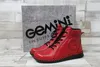 A pair of red leather ankle boots are displayed in front of their packaging. Produktbild-Vorschau