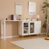 A white sideboard with glass doors and gold legs is placed against a light beige wall, with a long white table attached to its left. Two framed Vogue posters hang on the wall above the furniture. A large rug covers the wooden floor in front of the sideboar Anteprima dell’immagine prodotto