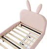 A close-up view of a pink upholstered bed frame with wooden slats and two black wire storage baskets underneath. Voir les images du produit