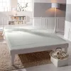 A white bed with a white fitted sheet is shown in a bright, minimalist bedroom. The bed is the main focus, with a white metal headboard and frame. The room has large windows, a bookshelf, and a floor lamp. Produktbild-Vorschau