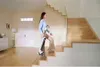 A woman is walking up a wooden staircase while holding a vacuum cleaner. Náhľad obrázku produktu