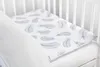 A baby blanket with a feather pattern is laid on a crib mattress. Anteprima dell’immagine prodotto
