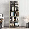 A tall, narrow bookshelf with black shelves and gold metal frame, filled with books and decorative items, set against a textured light gray and white wall. Produktbild-Vorschau
