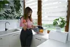 A woman is in a kitchen, holding an apple and looking at a food storage container filled with fruits and vegetables. Voir les images du produit