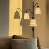 A floor lamp with three rattan shades casts shadows on a wall, next to a sofa with pillows. Anteprima dell’immagine prodotto
