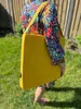 A person wearing a colorful floral shirt is carrying a large yellow bag outdoors on a grassy lawn. Náhled obrázku produktu