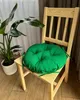 A green round cushion is placed on a wooden chair next to a potted plant. Produktbild-Vorschau