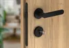 A close-up of a black door handle and lock set on a wooden door. Produktbild-Vorschau