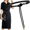 A woman wearing a black dress and a black belt, holding a black purse. Náhled obrázku produktu