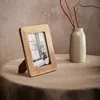A wooden picture frame with a photo inside, placed on a table next to a vase with branches. Podgląd zdjęcia produktu