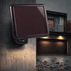 A solar-powered LED floodlight with a motion sensor is mounted on a textured wall, with a modern house and garage visible in the background. Produktbild-Vorschau