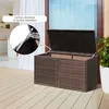 An outdoor storage box with its lid open, showing a close-up of the hydraulic support mechanism. The box is on a wooden deck next to a glass door and a potted plant. Produktbild-Vorschau