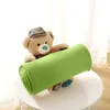 A teddy bear wearing a hat holds a rolled-up green blanket. Produktbild-Vorschau