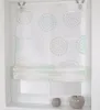 A white Roman blind with a circular pattern in turquoise and beige, hanging in a window frame. Produktbild-Vorschau