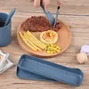 A person is using a blue plastic fork and knife to cut a steak on a wooden plate, which also contains french fries, pasta, and corn. A blue cup with a spoon and a blue cutlery case are also visible. Produktbild-Vorschau