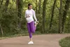 A pregnant woman is stretching outdoors on a paved path surrounded by trees. Náhled obrázku produktu