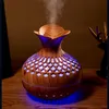 A wooden-patterned essential oil diffuser emitting mist, with blue LED lighting at its base. Produktbild-Vorschau