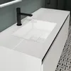 A modern bathroom vanity with a white countertop and sink, featuring a black faucet. The vanity has a textured side panel and is set against a muted green wall. Produktbild-Vorschau