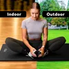 A woman is sitting on a yoga mat in a split image, with one side showing an indoor gym setting and the other side showing an outdoor park setting. Podgląd zdjęcia produktu