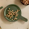 A green digital kitchen scale with hazelnuts on it, next to a bowl of hazelnuts. Produktbild-Vorschau