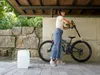 A woman is cleaning a bicycle with a handheld pressure washer. Produktbild-Vorschau