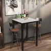 A bar table with two stools in a modern setting, with bottles of alcohol and a plant on the table. Náhľad obrázku produktu