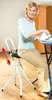 A woman is ironing clothes while sitting on a special stool next to an ironing board. Náhľad obrázku produktu