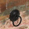 A close-up of a black metal drawer pull with a ring handle attached to a weathered wooden surface. Anteprima dell’immagine prodotto