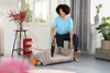 A woman is using a handheld vacuum cleaner on a dog bed in a living room. Produktbild-Vorschau