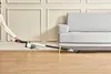 A person is using a cordless vacuum cleaner to clean under a sofa. Produktbild-Vorschau