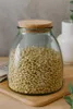 A glass storage jar filled with pine nuts, sealed with a cork lid, sitting on a wooden cutting board. Produktbild-Vorschau
