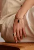 A person's hand wearing a bracelet with a gummy bear charm and rings, resting on a beige fabric. Produktbild-Vorschau