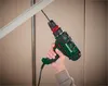 A hand holding a green and black drill, drilling into a ceiling. Anteprima dell’immagine prodotto