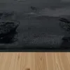 A close-up view of a black shaggy rug on a wooden floor. Voir les images du produit
