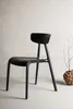 A black chair is shown in a studio setting against a textured wall and a light gray floor. Podgląd zdjęcia produktu