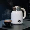 A white electric kettle is shown steaming next to a cup of coffee on a dark countertop. Náhľad obrázku produktu